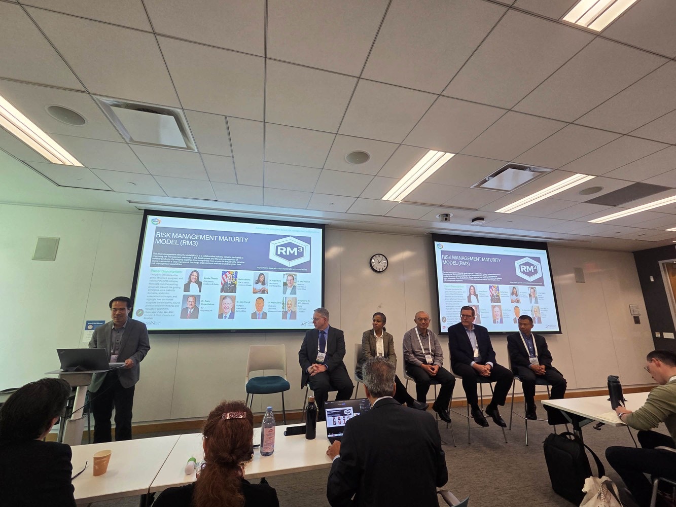 The RM3 panel session in progress, with panelists seated before two presentation screens.